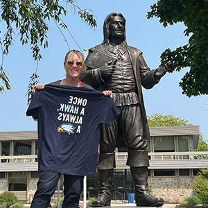 Kelly Scafariello拿着一把“Once a Hawk”, always a Hawk" T-shirt by the Roger Williams statue on Bristol Campus